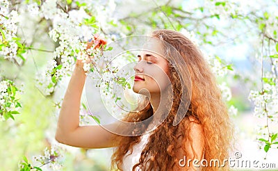 Beautiful young woman enjoys smell spring flowers over garden Stock Photo