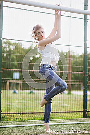 Beautiful young woman on a green football field. Girl standing at football gate, dressed in blue jeans, a white t-shirt Stock Photo