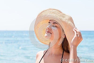 Beautiful young woman in hat is applying sunblock under her eyes and on her nose like Indian. Sun protection concept Stock Photo