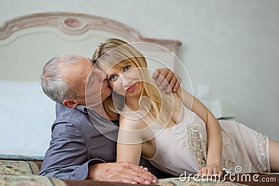 Beautiful Young Woman with Her Senior Lover Lying on the Bed. Man Kissing His Girlfriend. Portrait of Happy Lovely Couple Stock Photo