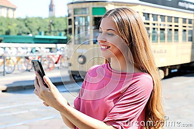 Beautiful young woman holding smart phone in her hands in street with old tram passing on the background in Milan, Italy Stock Photo