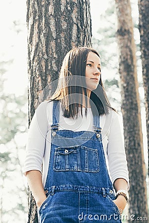 Beautiful young woman in jeans overalls standing in woodland Stock Photo