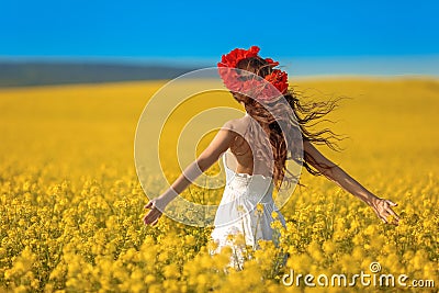 Beautiful young woman with long healthy hair over Yellow rape field landscape background. Attracive brunette girl with red poppy Stock Photo