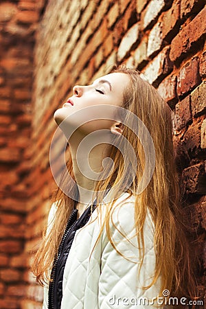 Beautiful young woman with long red hair stands near the red wall street in the city Stock Photo