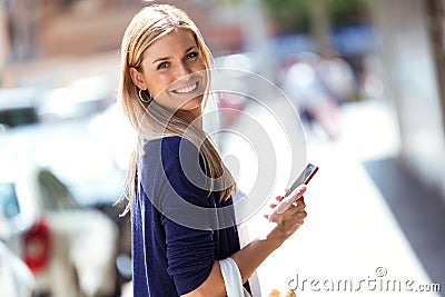 Beautiful young woman looking at the camara while using her smarrtphone in the street. Stock Photo