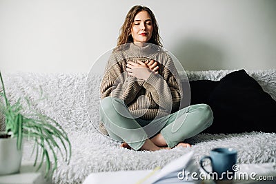 Beautiful young woman in lotus pose on bed practicing pranayama breathing techniques, finding inner balance after a Stock Photo