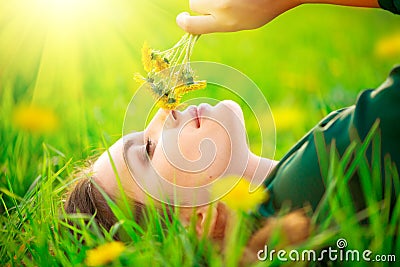 Beautiful young woman lying on the field in green grass and smelling blooming dandelions. Allergy free Stock Photo