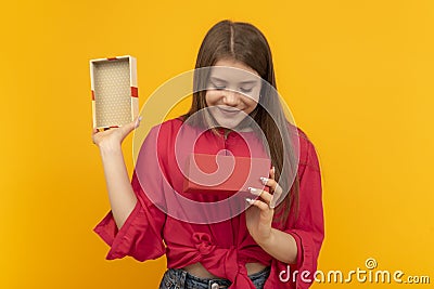 Beautiful young woman with an open gift box and looks admiringly into it. Girl received gift. Yellow background Stock Photo
