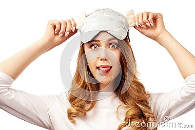 A beautiful young woman in pajamas and a sleep mask foolishly shows her tongue and makes a surprised look. Stock Photo