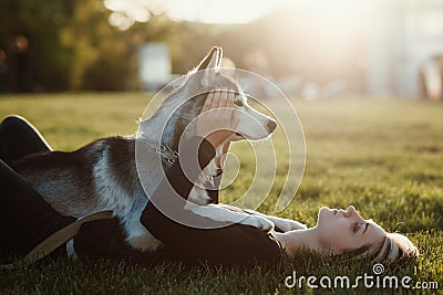Beautiful young woman playing with funny husky dog outdoors in park at sunset or sunrise Stock Photo