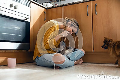 Beautiful young woman playing with her cute lovely animals sitting on the floor in the kitchen at home Stock Photo