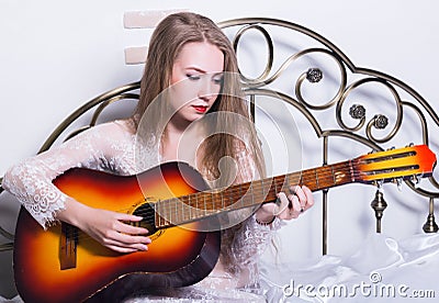 Beautiful young woman playing music on a bed with happiness and guitar Stock Photo