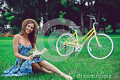 Beautiful young woman portrait reading a book with bicycle in the park. Stock Photo