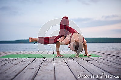 Beautiful young woman practices yoga asana Parivritta Eka Pada Danda Kaundiniasana on the wooden deck near the lake Stock Photo