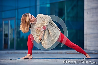 Beautiful young woman practices yoga asana Parivritta Parshvakonasana - Revolving side angle posture outdoors against the Stock Photo