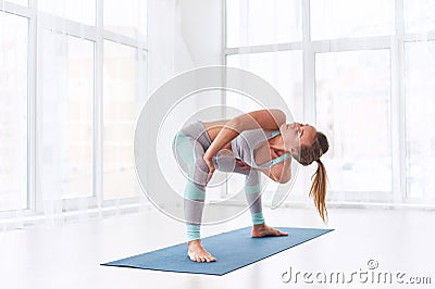 Beautiful young woman practices yoga asana Parivritta Stupasana at the yoga class Stock Photo