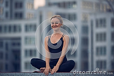 Beautiful young woman practices yoga asana Sukhasana - The Easy Sitting crosslegged Pose outdoors against the background of a mode Stock Photo