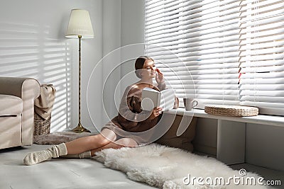 Beautiful young woman reading book near window. Winter atmosphere Stock Photo