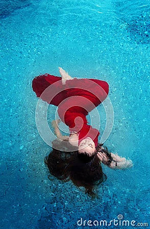 Beautiful young woman in red evening dress elegant floating weightlessly in the water in the pool dark brown curly hair floating Stock Photo