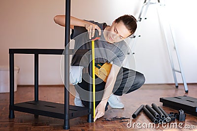 Beautiful young woman repairman measures the length of the shelf with a tape measure while making repairs in the house Stock Photo