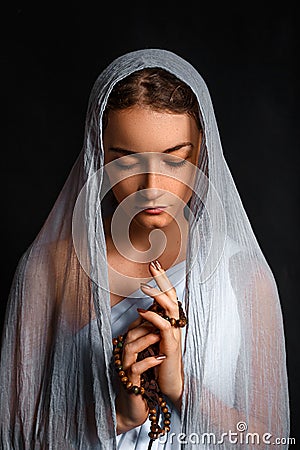 Beautiful young woman with a scarf on her head, and a rosary in her hands, humble look, believing woman Stock Photo