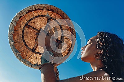 Beautiful young woman with shaman drum outdoors and playing ethnical music Stock Photo