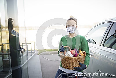 Beautiful young woman is shopping with mouth protecting mask during corona covid crisis and is holding her shopping basket Stock Photo