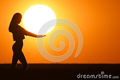 Beautiful young woman silhouette at sunset. The girl is holding the big day in her hands. Stock Photo