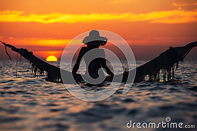 Beautiful young woman silhouette with swing posing in the sea on sunset, maldivian romantic scenery Stock Photo