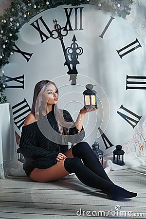 Beautiful young woman sitting on the background of a large clock Christmas decor, holding a flashlight, waiting for the holiday Stock Photo