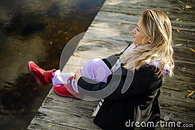 Beautiful young woman sitting on the edge of wooden jetty by the lake with autumn reflections Stock Photo