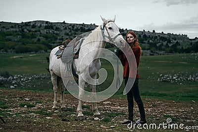 Beautiful young woman standing in the mountains and holding a white horse, nature Stock Photo