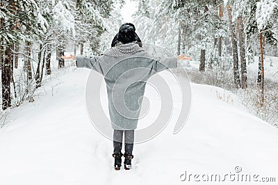 Beautiful young woman standing among snowy trees in winter forest and enjoying snow. Stock Photo