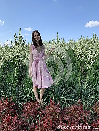 A beautiful young woman stands in the face of huge tall flowers. Stock Photo