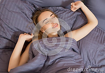Beautiful young woman stretching after waking up while in cozy bedroom bed, smiling rested girl feeling refreshed sitting on white Stock Photo