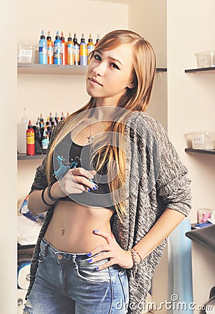 Beautiful young woman tattoo artist portrait with tattoo machine against tattoo ink bottles. Stock Photo
