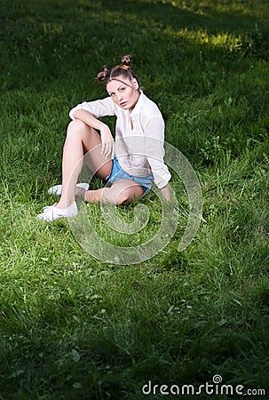 Beautiful young woman in trendy casual clothes sitting on the grass Stock Photo