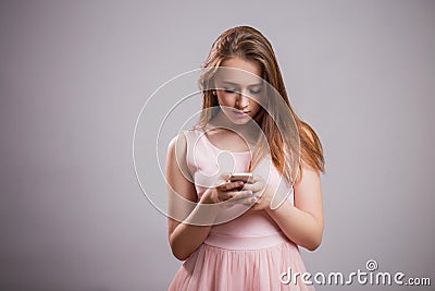 Beautiful young woman wears pink dress and uses smartphone on grey background with copy space Stock Photo