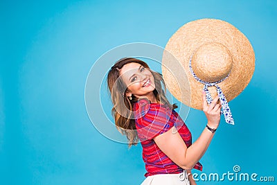 Beautiful young woman wears in summer dress and straw hat is laughing on blue background with copy space Stock Photo