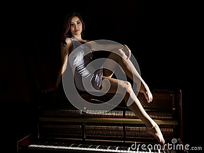 Beautiful young woman in a white dress with an open back sitting on a old piano on a dark background Stock Photo