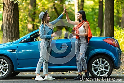 Beautiful young women giving high five, having fun together, cheering with raised arms driving modern convertible car on summer Stock Photo