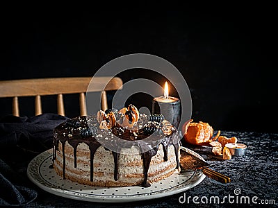Beautifully styled and decorated birthday cake with one candle lit up, on a table with chair in the background,oranges, walnut and Stock Photo