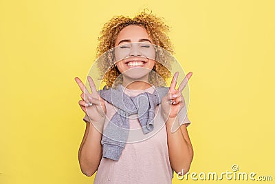 Beautifyl girl is smiling and showing a piece symbol with fingers on her hands. Isolated on yellow background. Stock Photo