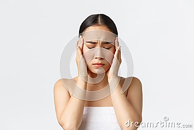 Beauty, cosmetology and spa salon concept. Young uneasy asian woman in bath towel feeling migraine, touching temples and Stock Photo