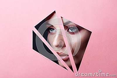 Beauty face red make-up eyes of a young girl in a slit hole of pink paper. Woman with beautiful makeup red glowing shadow, plump Stock Photo