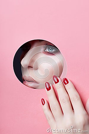 Beauty face red makeup plump lips red nails of a young girl in a round slit hole of pink paper. Woman with beautiful makeup plump Stock Photo
