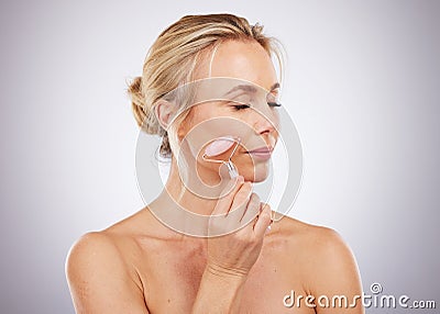 Beauty, face roller and woman doing massage in studio with dermatology and cosmetic tools. Mature aesthetic model skin Stock Photo