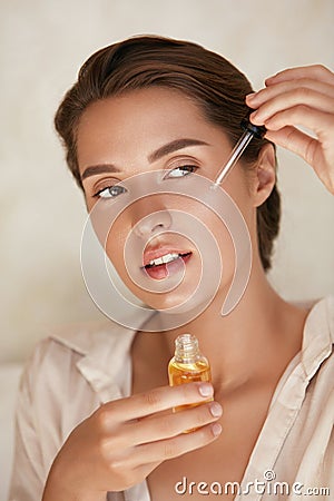 Beauty Face. Woman Applying Essential Oil On Facial Skin And Looking Away. Beautiful Model Moisturizing Derma. Stock Photo