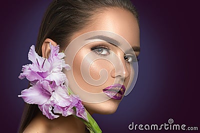 Beauty fashion brunette girl with gladiolus flowers. Glamour woman with perfect violet trendy makeup Stock Photo