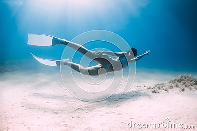 Beauty lady freediver underwater glides with white fins. Attractive woman freediver in blue ocean with sun rays Stock Photo